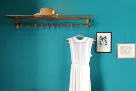 Hanger with straw hat and white dress near blue wall